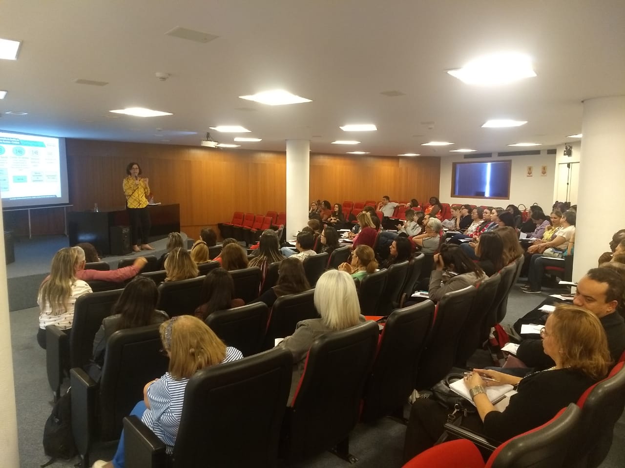 Foto do auditório da EMASP durante o curso. No palco, a instrutora Valéria Pugliese, coordenadora da COGESS